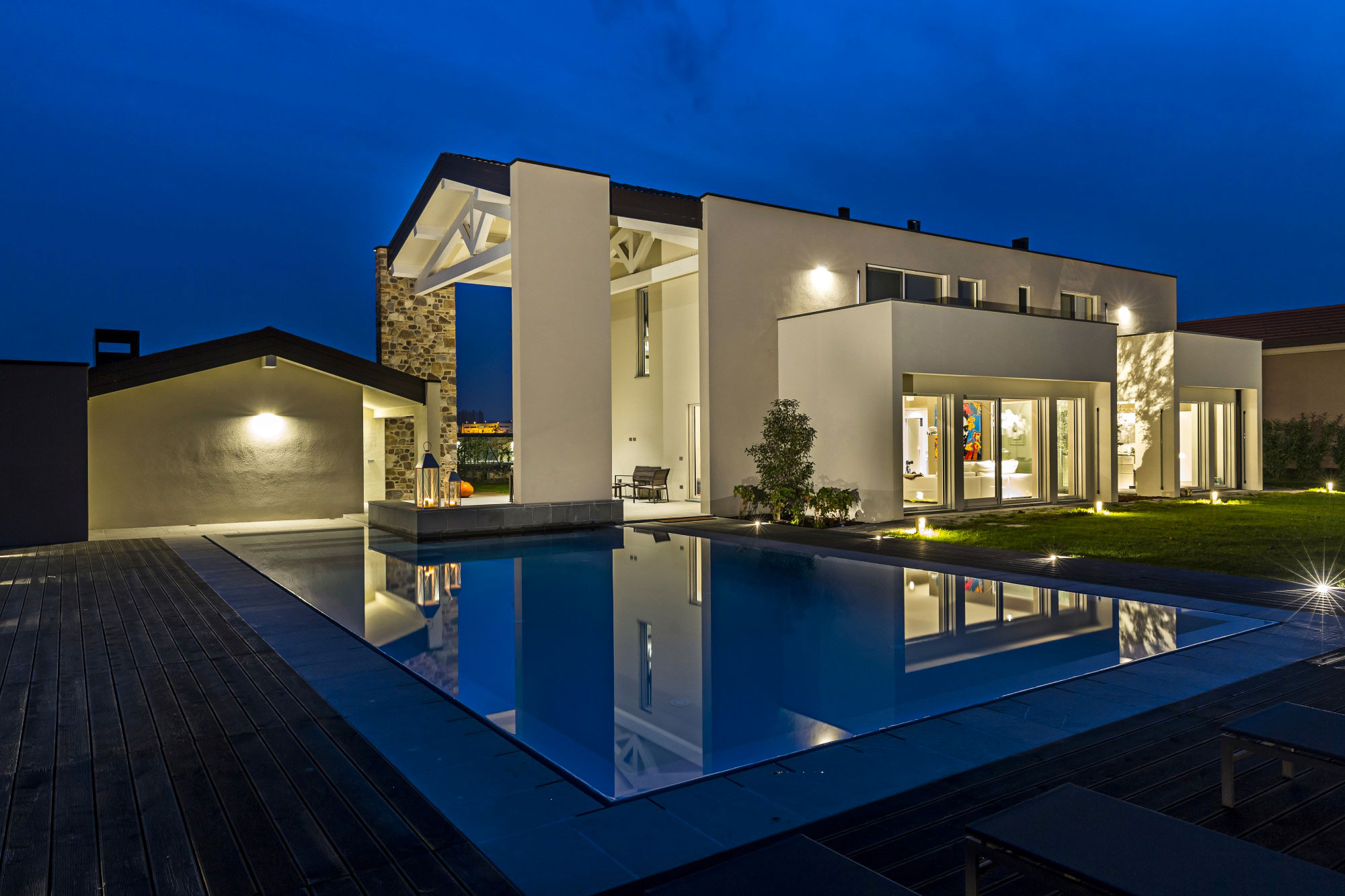 Imagen de noche con una casa iluminada, junto al jardín y la piscina